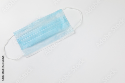 Coronavirus prevention typical 3-ply blue surgical medical mask with rubber ear straps on white background. Hygiene corona virus protection concept. Flat lay, copy space.