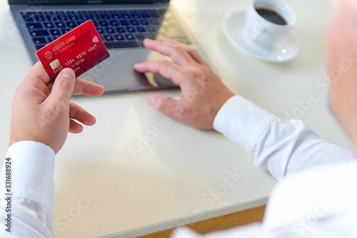 Closeup of caucasian hand, holding a gold credit card and tyoing on a laptop photo