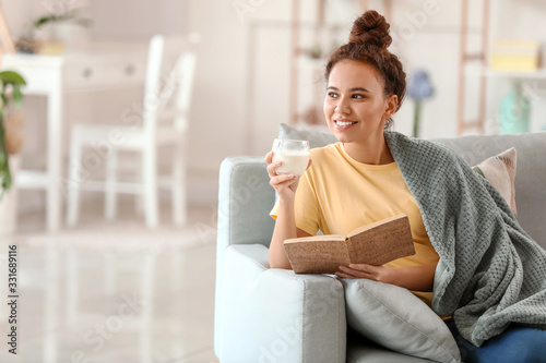 Young African-American woman with milk reading book at home