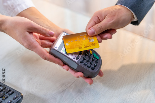 Closeup of caucasian right hand, holding gold credit card on a PIN PAD held by a woman's hands photo