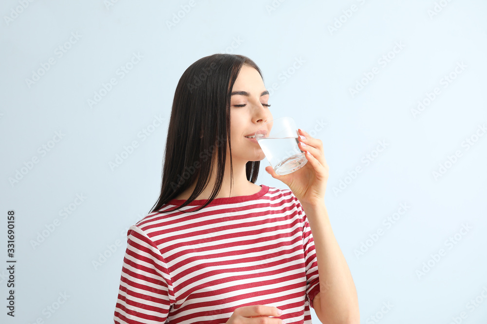 Beautiful young woman drinking water on color background