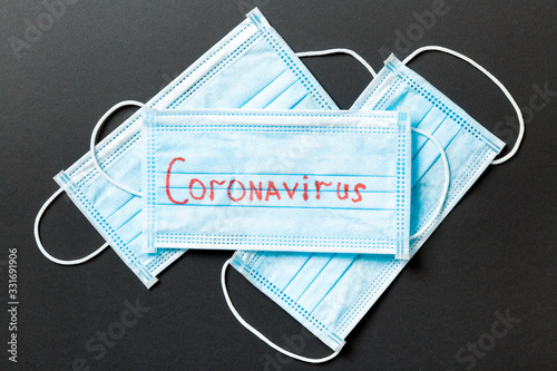 Epidemic background made of coronavirus word on heap of protective medical masks on black background. World quarantine concept