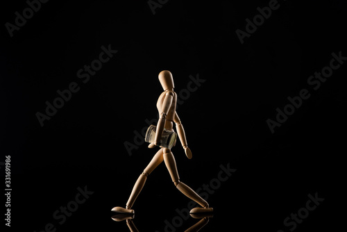 Wooden doll imitating walking with money on black background