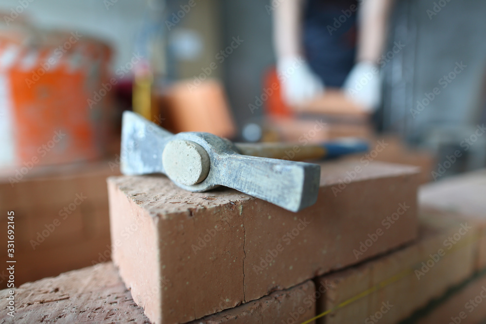 Focus on structure utensil lying on big red bricks. Smart man using helpful tool to make big and stable concrete wall made of hard blocks. Building concept