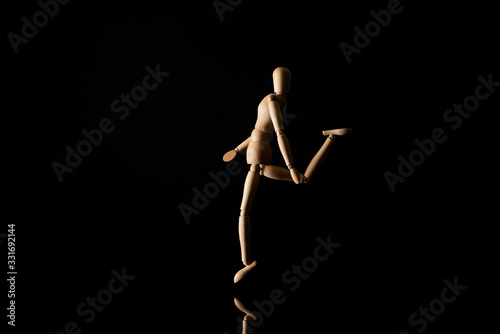 Wooden doll imitating raising leg on black background