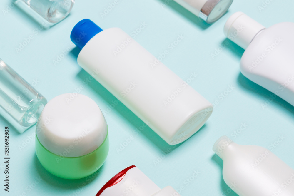 Close-up set of diffrent sized bottles and jars for cosmetic products on blue backgound. Face and body care concept with copy space Close-up set of diffrent sized bottles and jars for cosmetic products on blue backgound. Face and body care concept with copy space