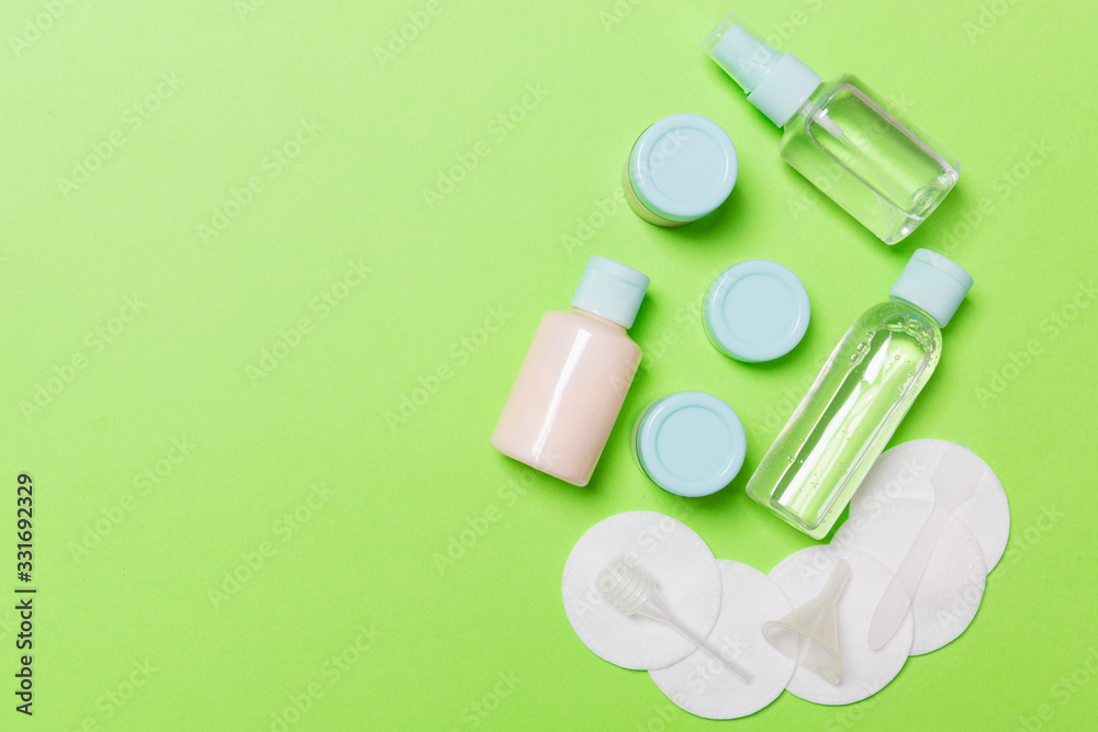 Group of small bottles for travelling on green background. Copy space for your ideas. Flat lay composition of cosmetic products. Top view of cream containers with cotton pads Group of small bottles for travelling on green background. Copy space for your ideas. Flat lay composition of cosmetic products. Top view of cream containers with cotton pads