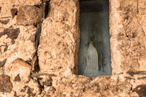 Statuette of the Virgin Mary in a small window of a medieval church on the background of masonry. Back view.