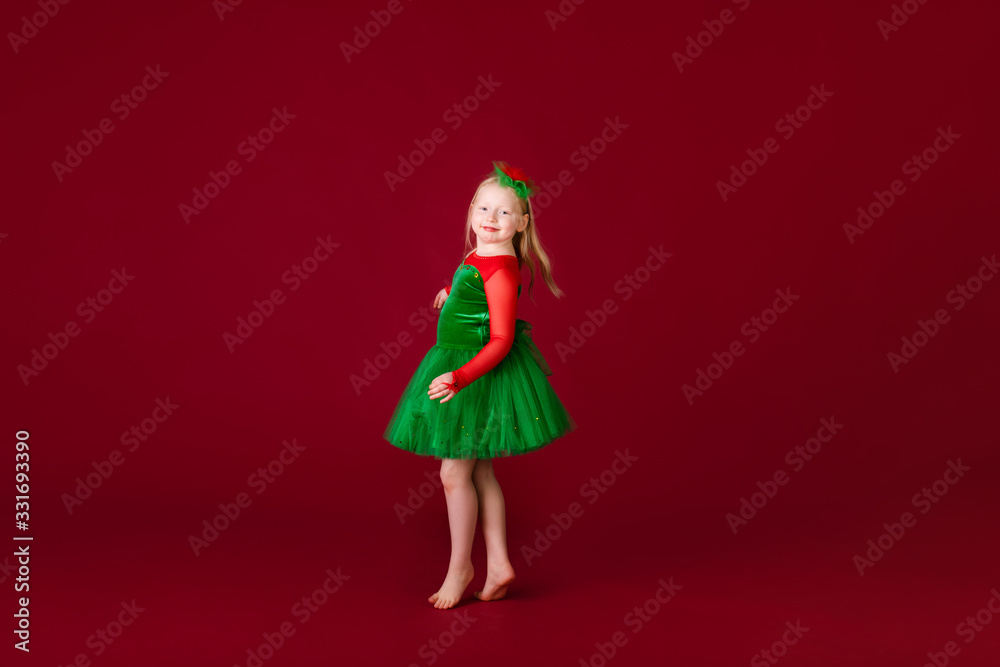 Little blonde girl in a christmas and new year green costume having fun and sending kisses on red background. Space for text. Dreams come true Merry Christmas
