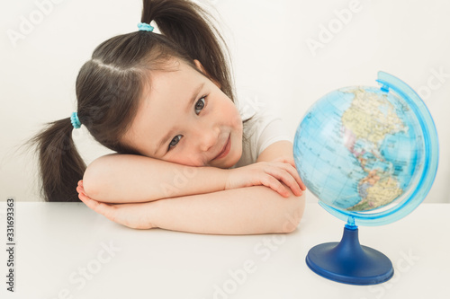 A girl is exploring the planet earth. A child is playing with a globe. Little girl is looking for her country on the globe