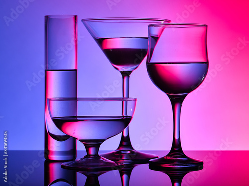 Different glass goblets on a red and purple background. Beautiful still life