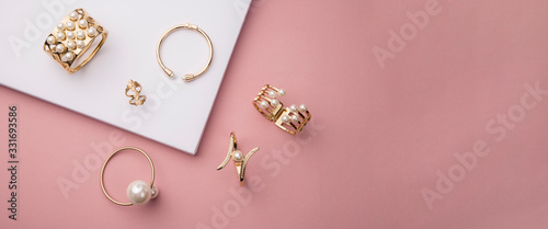 Fotografia Top view of golden with pearl bracelets on pink and white background with copy s