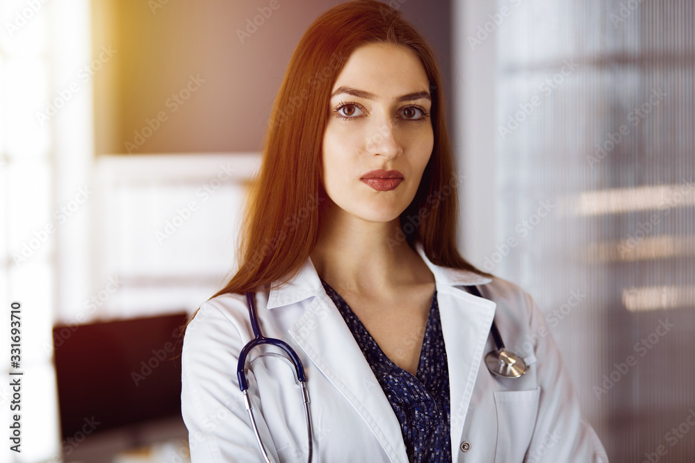 Cheerful smiling female doctor standing with arms crossed in clinic. Portrait of friendly physician woman. Medicine concept Cheerful smiling female doctor standing with arms crossed in clinic. Portrait of friendly physician woman. Medicine concept