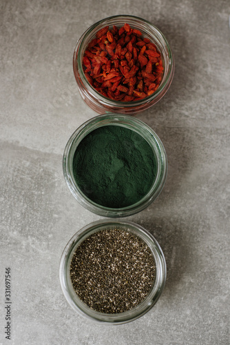 Different superfoods ingredients. Spirulina,chia, goji in glass jar on grey background