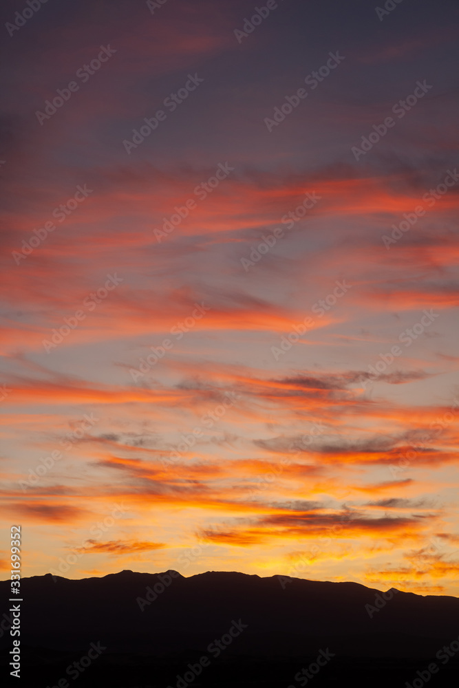 Sunrise in the sky inside the Death Valley desert land, nobody around, silence, a breathtaking sky with pink orange clouds, vertical view, and a silhouette of a mountain i