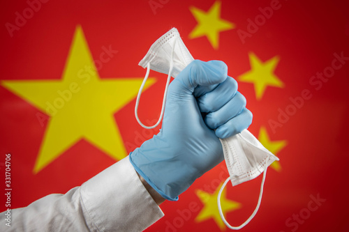 Hand with a glove holding a mask and the Chinese flag in the background Covid19 concept Selective focus