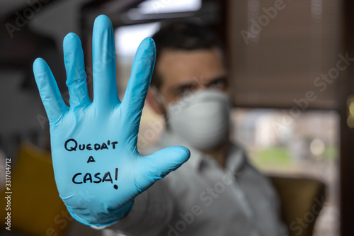 Young man with an open palm with a glove and a mask written in the Catalan language stay at home quarantine concept coronavirus
