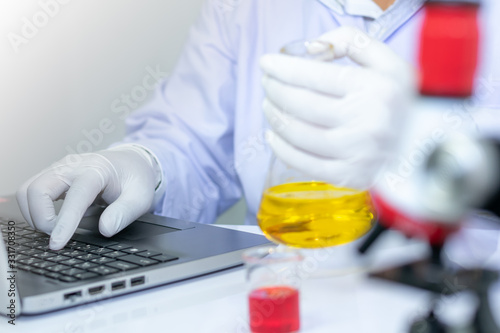 Close up scientists' hands are recording the results of the science experiment on a laptop computer in the lab, Concept of research and medical science.