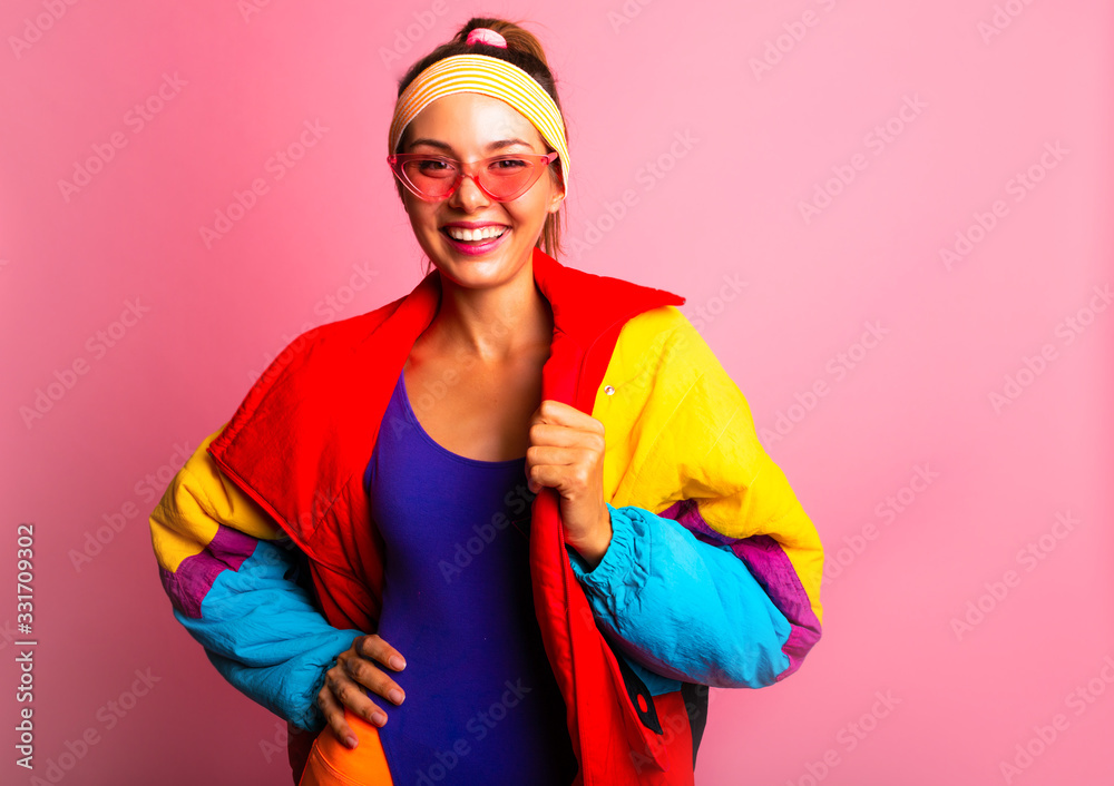Back in time 90s 80s. Stylish girl in retro colourful vintage coat, orange  leggings, and purple body, fashion trends, entertainment. 80's Fashion woman  over pink background. Beautiful athletic girl. Stock Photo