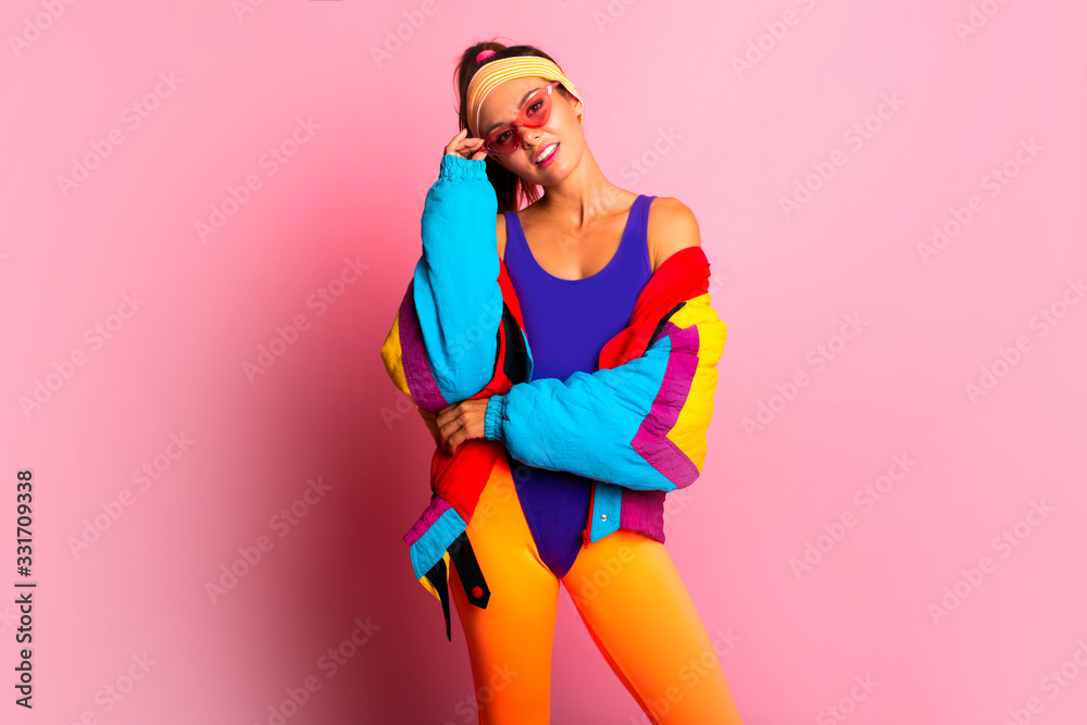 Back in time 90s 80s. Stylish girl in retro colourful vintage coat, orange  leggings, and purple body, fashion trends, entertainment. 80's Fashion woman  over pink background. Beautiful athletic girl. Stock Photo