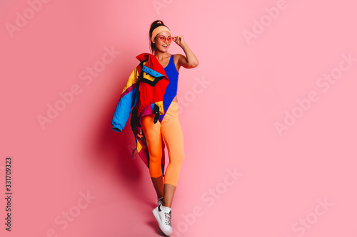 Full length fashion portrait of young trendy woman in cap and jeans looking away.young and cool, hipster girl with colored coat, orange leggings  and body suit. 80s 90s style