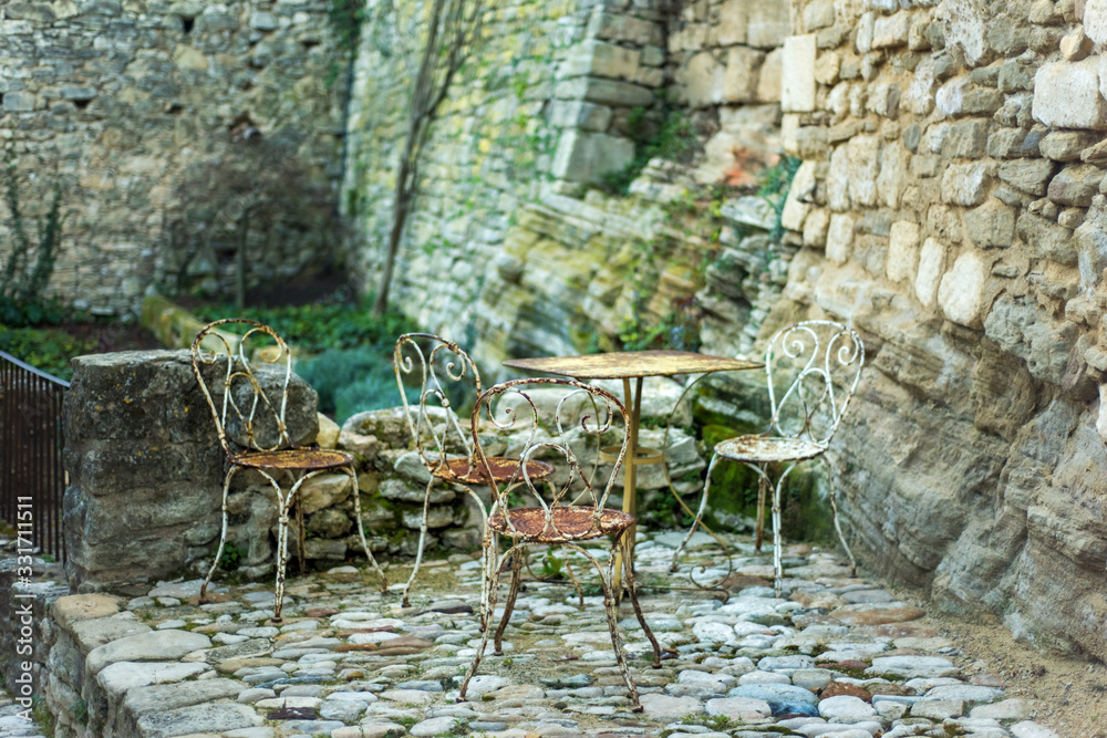Rusty empty old table and chairs on stone medieval terrasse in one of the most beautiful village of France Lacoste in Vaucluse, Provence, without tourists in low season. Bad time for travel Rusty empty old table and chairs on stone medieval terrasse in one of the most beautiful village of France Lacoste in Vaucluse, Provence, without tourists in low season. Bad time for travel