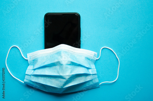 Blue medical mask on a black smartphone. Protection, disinfection of the smartphone. The mask is dressed on a smartphone on a blue, black, pink, yellow background. Copy Space. COVID-19