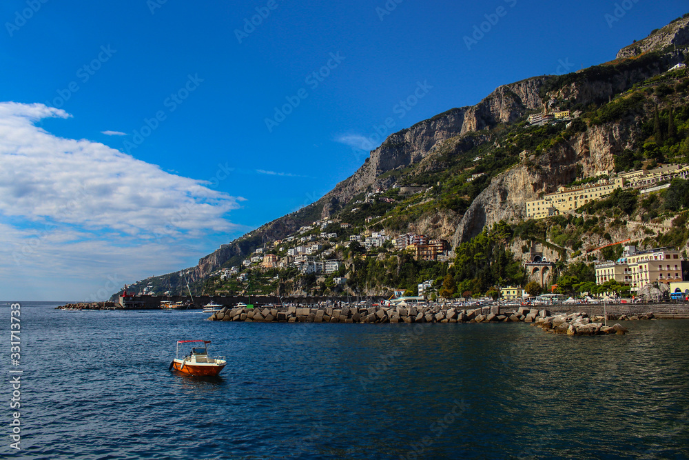 View of the town of Amalfi from the jetty with, the sea, boats and colorful houses on the slopes of the Amalfi coast in the province of Salerno, Campania, Italy.