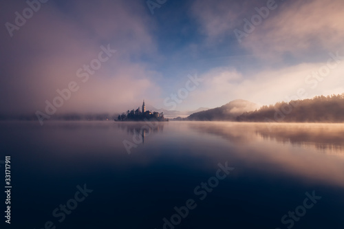 Amazing view on a misty morning of lake Bled with St. Marys Church of the Assumption on the small island  Bled, Slovenia, Europe. © pmartike