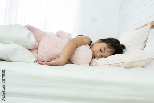 Portrait of a little girl sleeping in bed with a pink teddy bear at home. Sweet dreams and happiness moments..