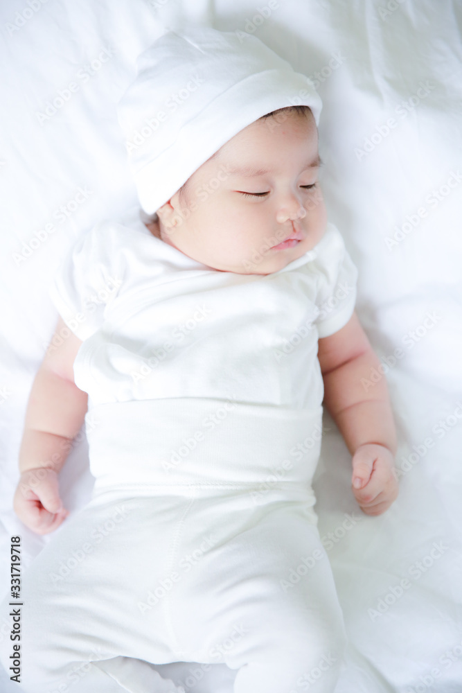 Portrait of a newborn Asian child wearing a white dress on a white mattress Portrait of a newborn Asian child wearing a white dress on a white mattress