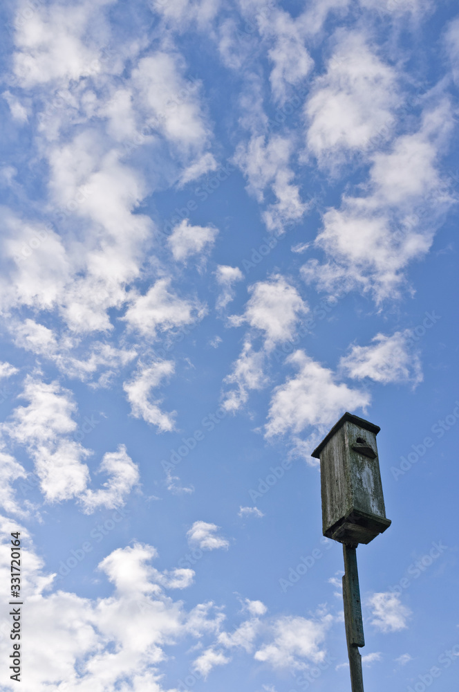 Rustic birdhouse on a background of sky with cirrus clouds. Waiting for Spring.