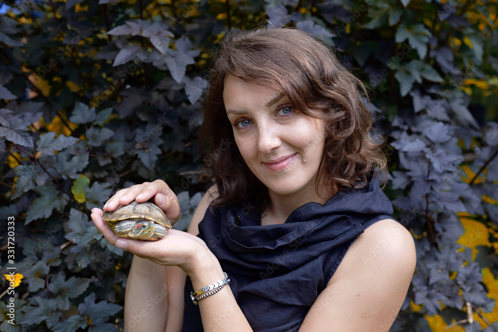 Portrait of smiling woman holding a little turtle. Young cute girl holds in hand the red-eared turtle. Portrait of smiling woman holding a little turtle. Young cute girl holds in hand the red-eared turtle.