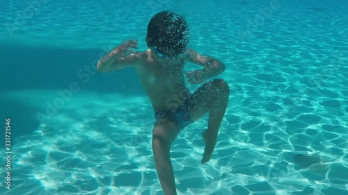 Little boy in swimming goggles dives under the water in the pool and wave his hands
