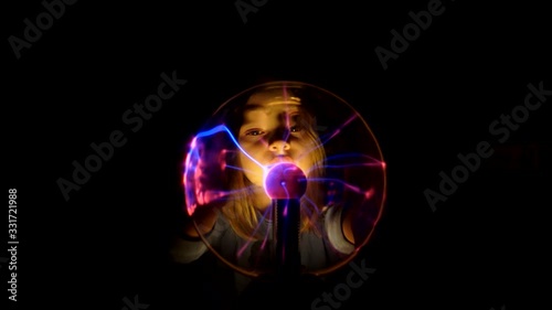 Pretty girl moves her fingers on the surface of the plasma tesla ball and watches for changes in condition photo