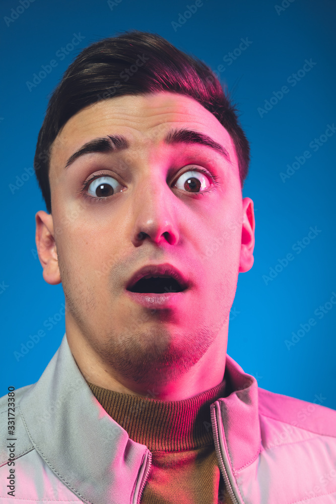 Astonished, looking on. Close up caucasian man's portrait isolated on blue studio background in pink neon light. Beautiful male model. Concept of human emotions, facial expression, sales, ad Astonished, looking on. Close up caucasian man's portrait isolated on blue studio background in pink neon light. Beautiful male model. Concept of human emotions, facial expression, sales, ad