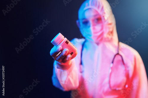 Holding cure pills for coronavirus. Nurse in mask and white uniform standing in neon lighted room