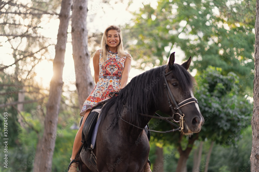 Young woman in a bright colorful dress riding a black horse Young woman in a bright colorful dress riding a black horse
