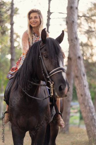 Young woman in a bright colorful dress riding a black horse © arthurhidden