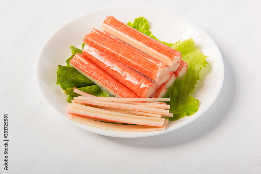 Crab sticks made of crab meat are placed on lettuce leaves, in delicate plates, isolated in white background Crab sticks made of crab meat are placed on lettuce leaves, in delicate plates, isolated in white background