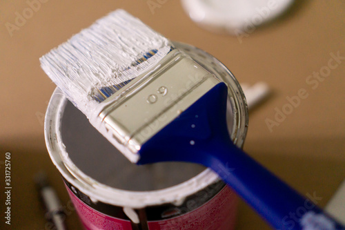 Dirty paintbrush sitting over a opened can with paint. Close up shot with rich details.