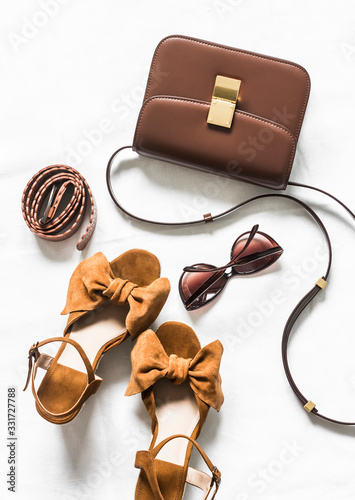 Cross body brown leather bag, suede wedge sandals and sunglasses on a light background, top view. Fashion concept