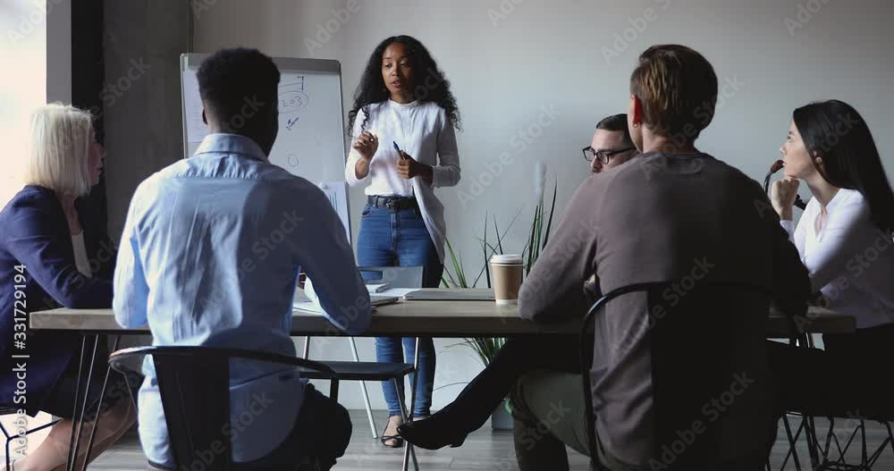 Focused motivated mixed race different ages business people listening to young african american female speaker in modern office. Successful professional biracial speaker holding educational lecture.