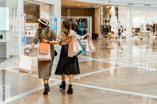 Shopping and entertainment, mall inside. Two beautiful girls with paper bags at the mall. The joy of consumption, Gift shopping, holiday.