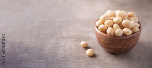 Macadamia nuts in wooden bowl on wood textured background. Copy space. Superfood, vegan, vegetarian food concept. Macro of macadamia nut texture, selective focus. Healthy snack. photo
