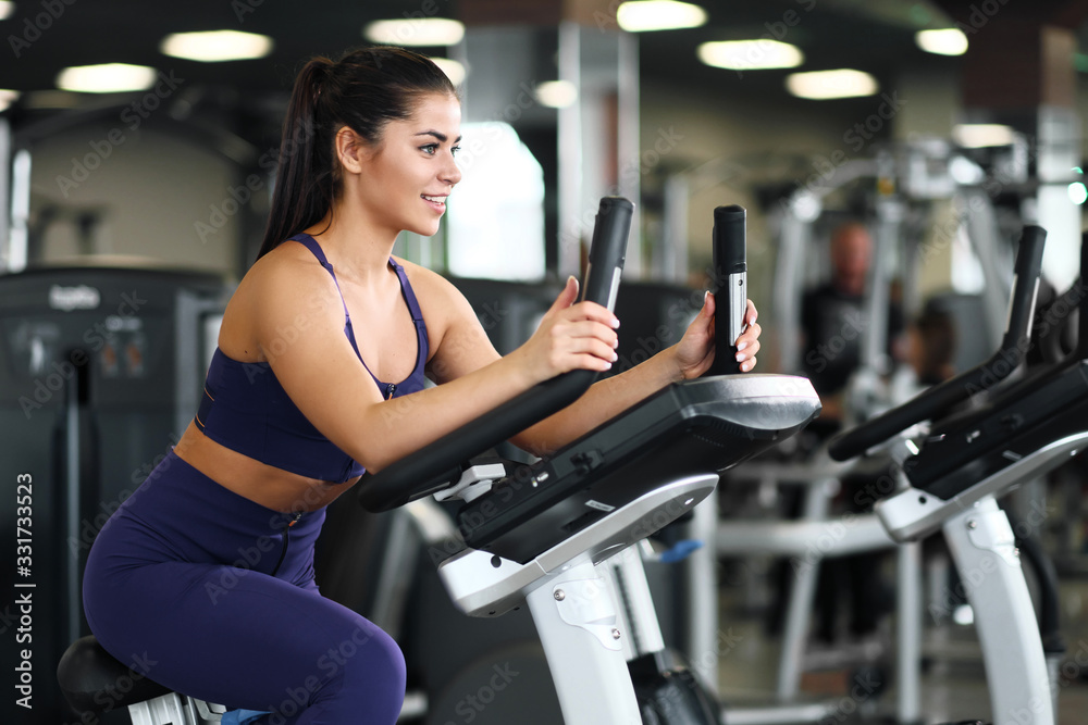 A beautiful athletic young brunette woman in sportswear in the gym is engaged on a bike. A beautiful athletic young brunette woman in sportswear in the gym is engaged on a bike.