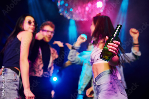 Girl holding bottle. Young people is having fun in night club with colorful laser lights © standret