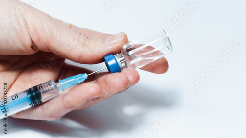 Doctor hand holds glass medicine bottle with injection fluid with blue aluminium caps and syringe for vaccination. Coronavirus epidemic, Cancer, painand diabetes, pharmaceutical medicine concept .