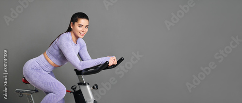 A beautiful athletic young brunette woman in sportswear trains on a sycle in ...