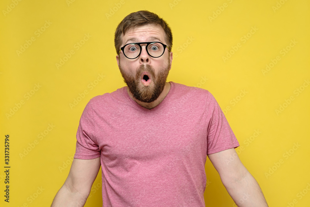 Man with glasses in shock, he opened mouth in surprise, looks with big eyes and spreads arms to the sides, on a yellow background. Man with glasses in shock, he opened mouth in surprise, looks with big eyes and spreads arms to the sides, on a yellow background.